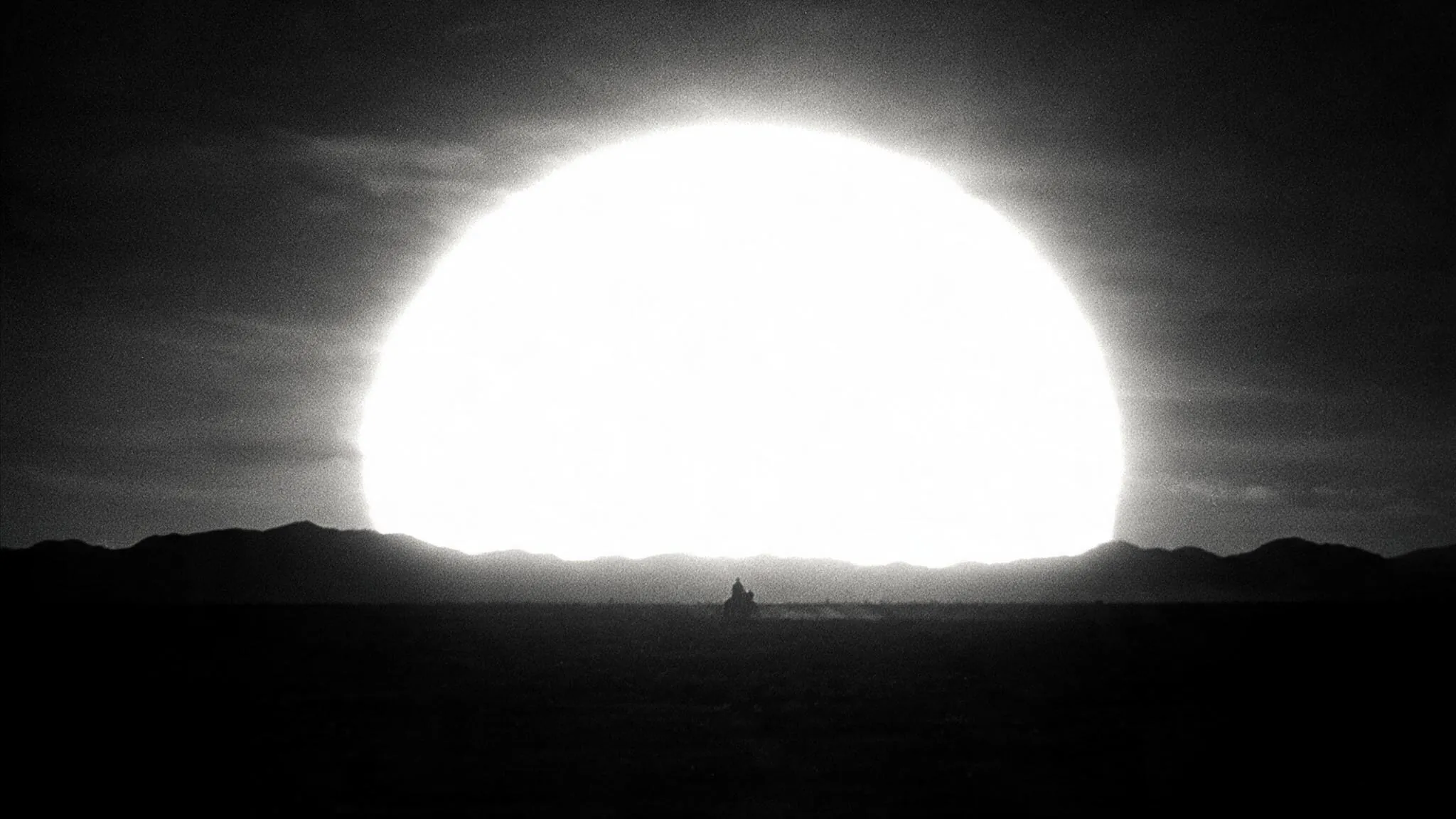 Storyboard frame: a lone rider crossing a plain, dwarfed by an enormous white sun on the horizon